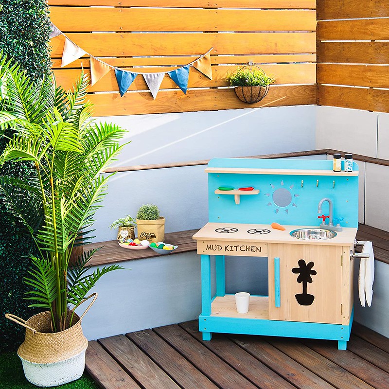 A Little Chef Outdoor Mud Kitchen in the outdoors, with a washing bowl, tap, towel rail and door.