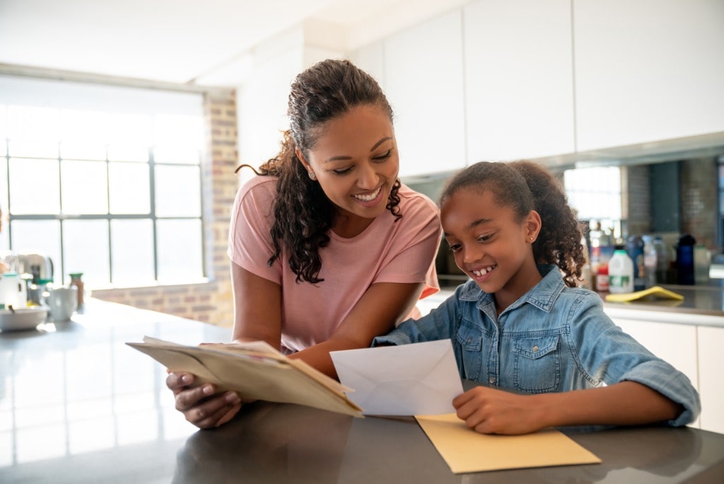 Mum and daughter standing in the kitchen smiling as they look through the post.