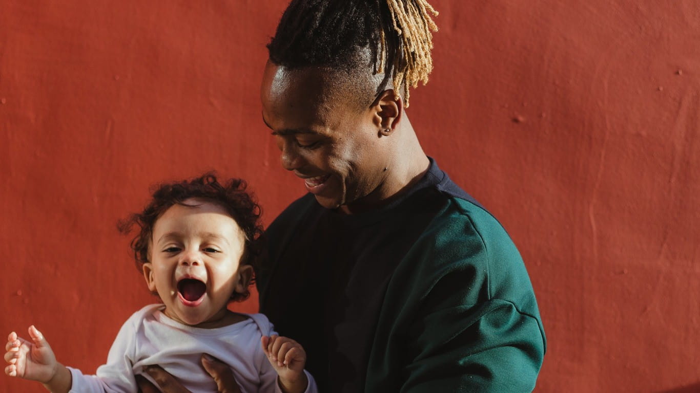 Dad holding his happy baby son in front of a brick red wall.
