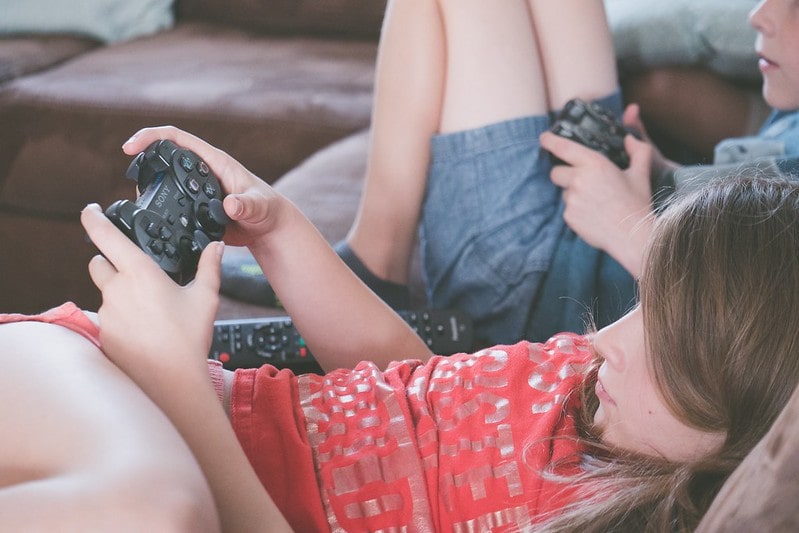 Brother and sister slumped on the sofa playing video games on their games console.