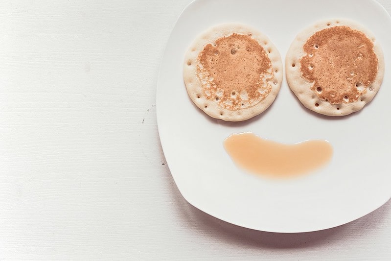 Plate with a smiley face using pancakes for eyes and syrup for a smile.