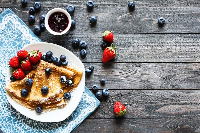 Plate of yummy folded crepes served with strawberries, blueberries and fruit compote.