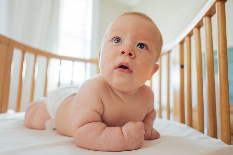 Baby boy in a diaper crawling in his wooden cot looking up at his parents.