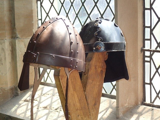 Two Iron Age helmets on a stand next to a window in a castle.
