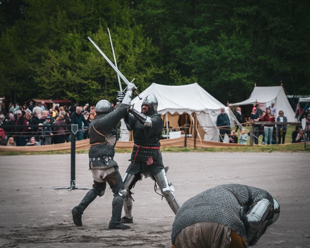 Medieval nights having a sword fight with spectators watching.