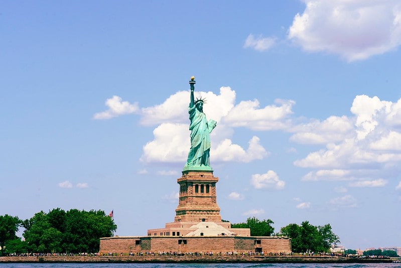 The Statue of Liberty on a bright day with blue skies and a few clouds.