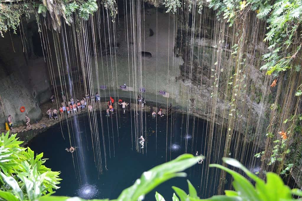 View of the sacred cenote from the top. People are swimming in the water.