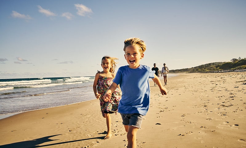 Kids laughing as they run along the beach.