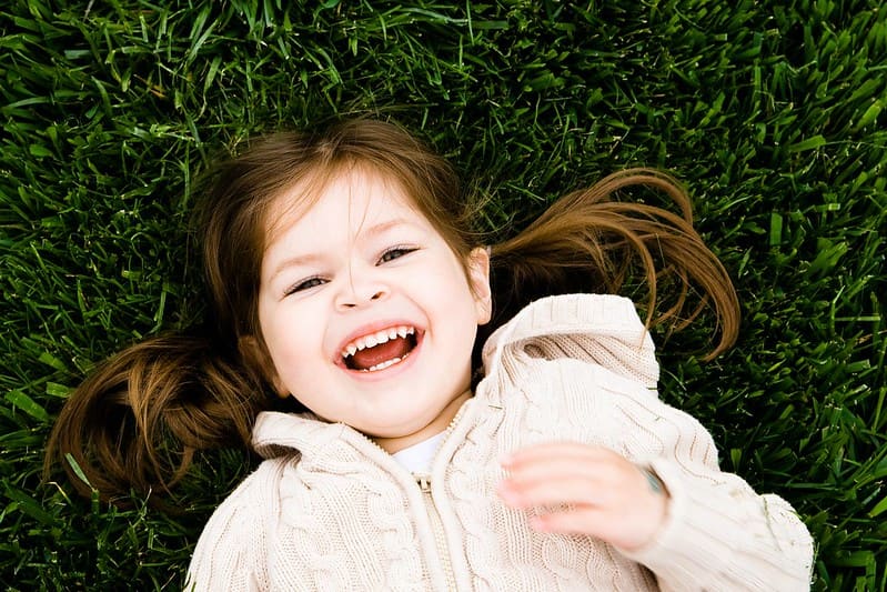 Little girl lying down in the grass laughing at pig jokes.