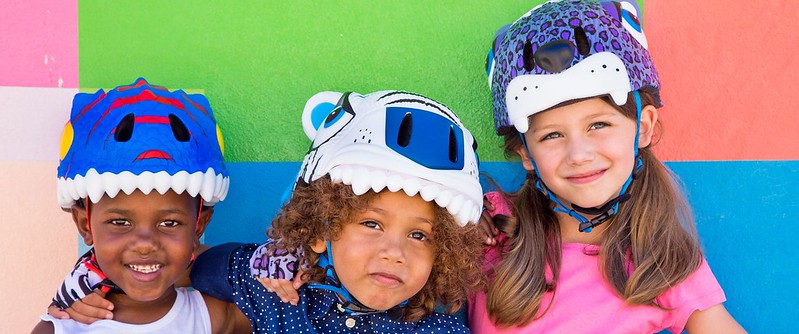 Three children wearing Crazy Safety Kids Bike Helmet shaped like a dinosaur, a cat and a bear.