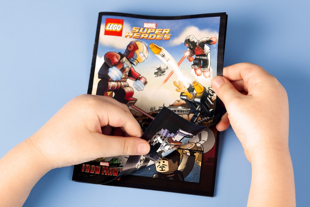 A child's hands opening a Lego Marvel Superheroes comic book.