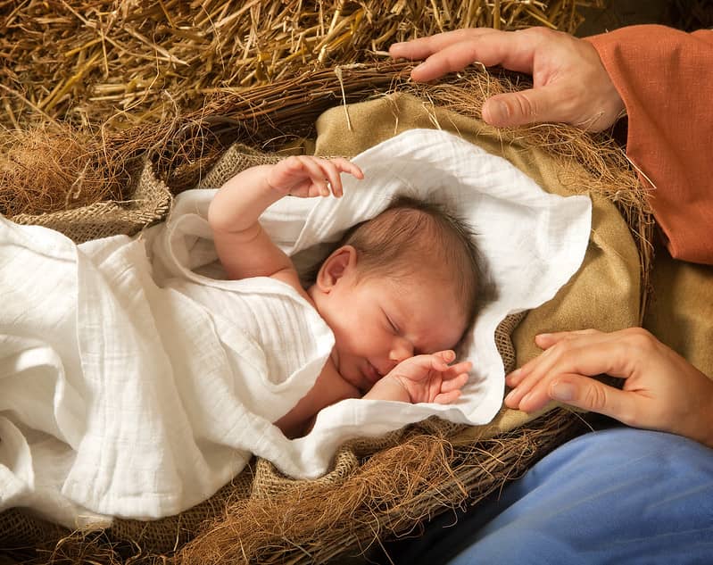 Newborn baby wrapped in white sheets in a manger.