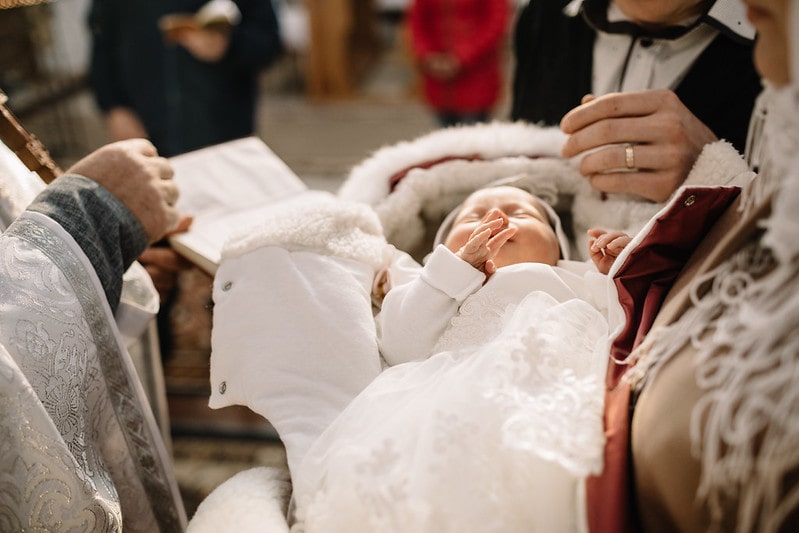 Baby dressed in white, lying in its parents' arms before the priest at its Christening.