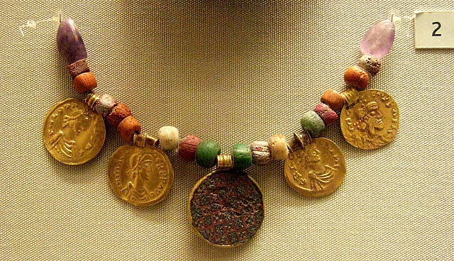 An Anglo-Saxon necklace, made from beads and large gold coins, hanging on display in a museum.