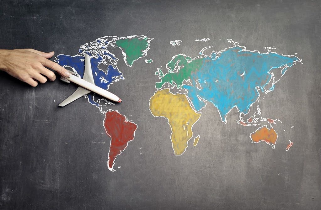 Map of the world drawn on a blackboard, the teacher moves a toy plane across it.