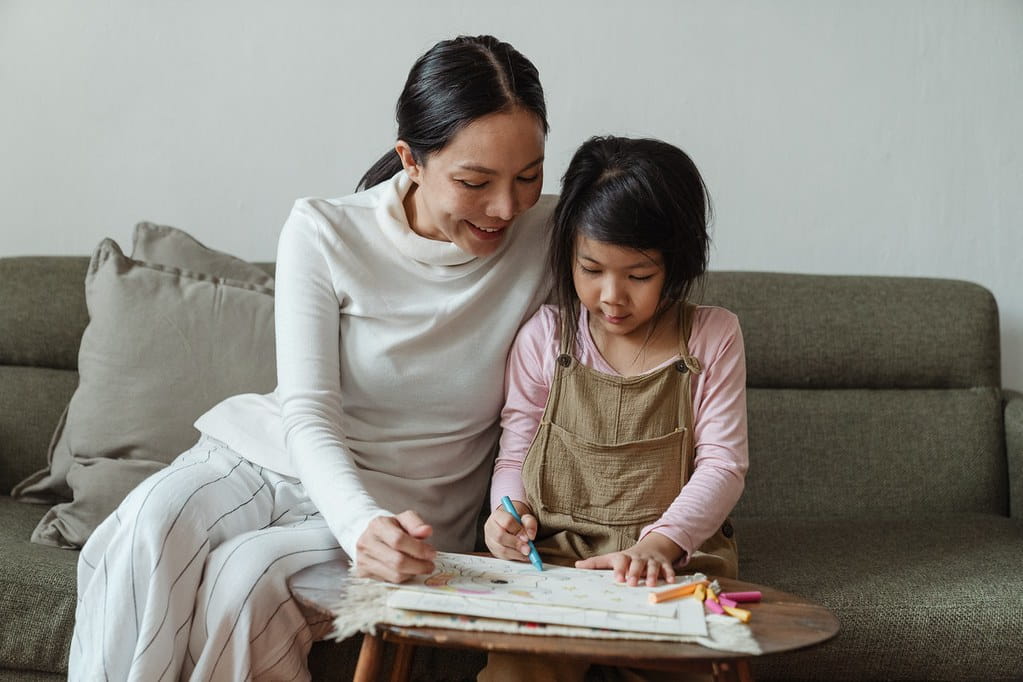 Mum and daughter sat on the sofa together drawing.