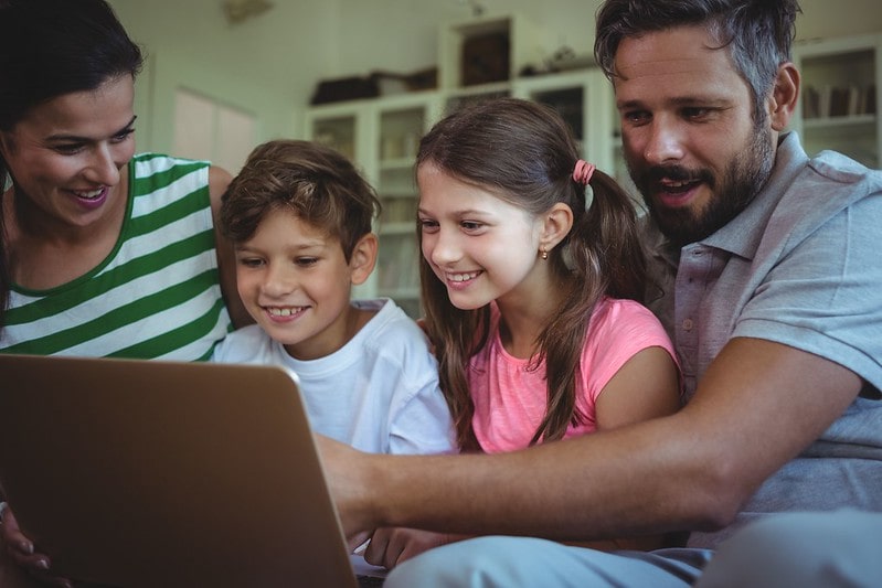 Parents sat with their two kids looking at a laptop to learn about ellipsis.