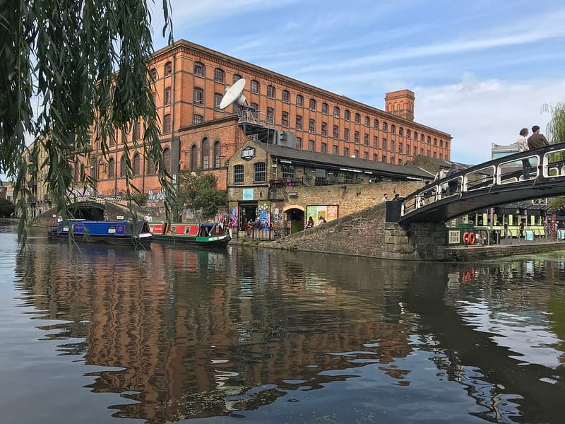Camden lock: the canal with barges and people walking across the bridge.