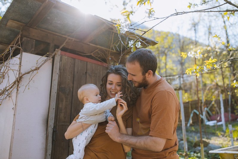 Parents in the garden holding their young baby and smiling.