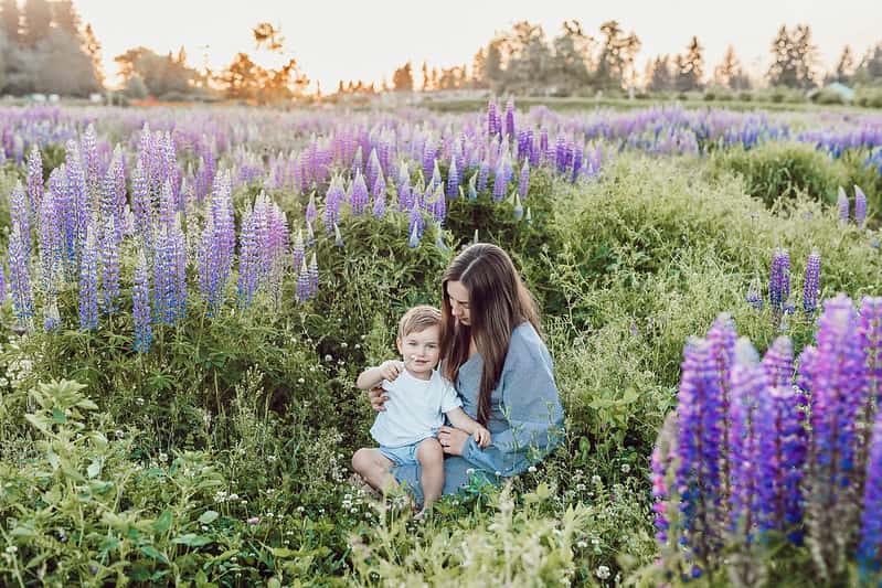Mum sitting with her baby son on her lap in a field of purple flowers.