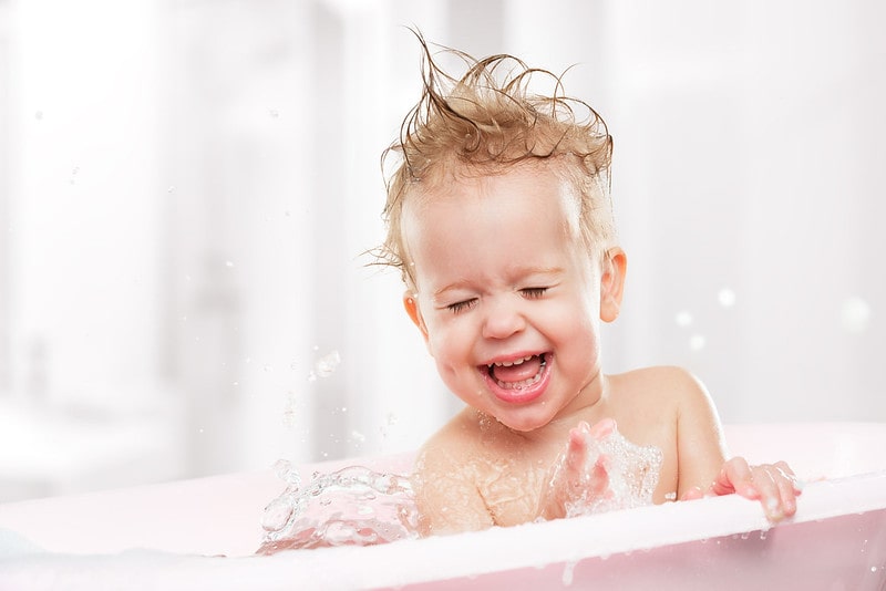 Happy baby laughing in the bath tub, bubbles splashing everywhere.