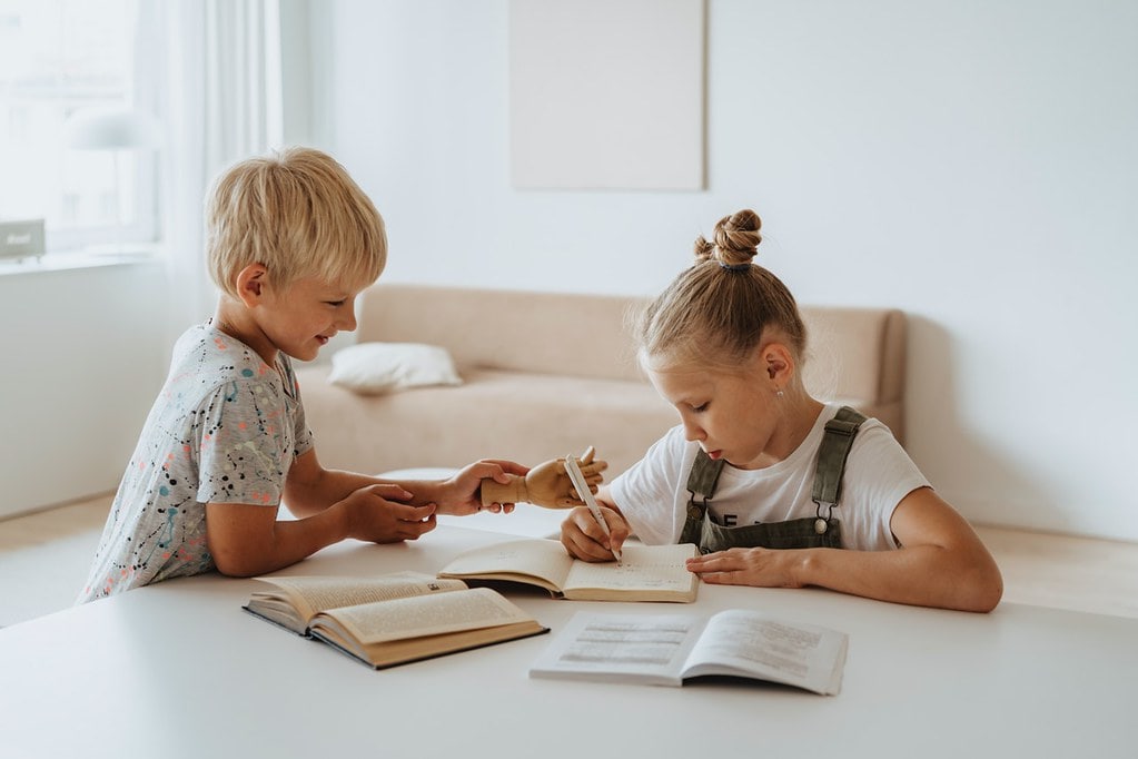Little girl and boy sat at the table writing about Roman inventions in their notebooks.
