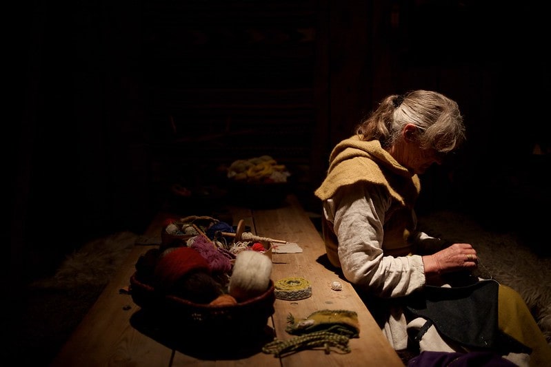 Viking woman sat at a table with weaving materials.