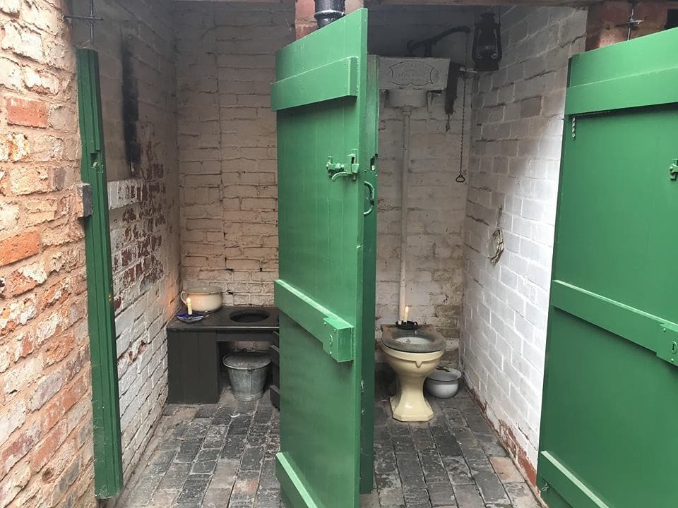 Victorian toilet cubicles with stone walls and green doors.