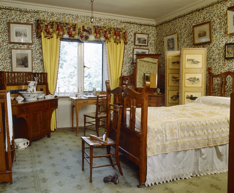 An upper-class Victorian bedroom with floral wallpaper and pictures on the walls.