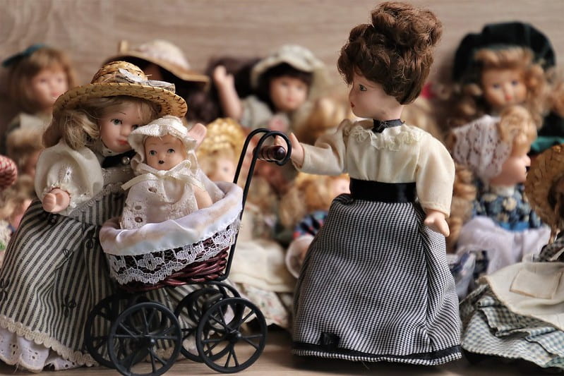 Dolls in dress from the Victorian era, one doll pushing a Victorian pram.