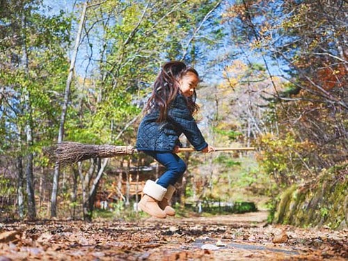 Little girl flying on a broomstick in the park.