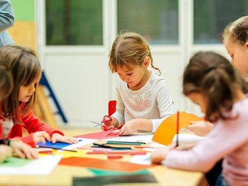 Little girls sat at the table doing origami.