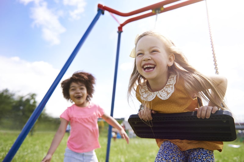 Two happy girls playing together on the swings at the playground.