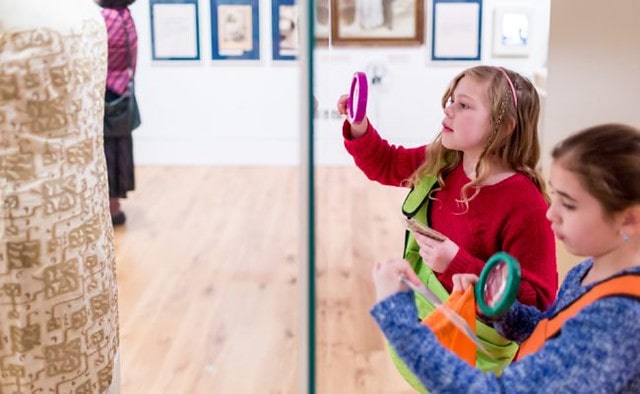 Two girls holding up magnifying glasses to an exhibit a The Jewish Museum.