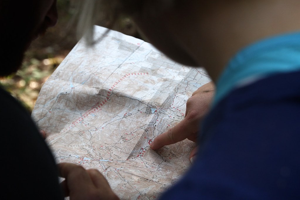 Child holding open a map, reading it and pointing to a location.