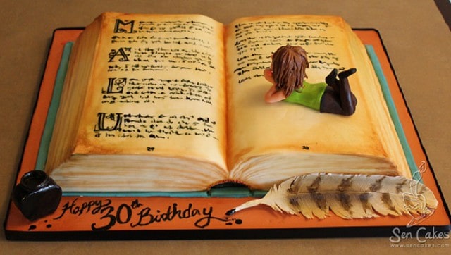 A book cake, pages open and a person figurine lying on the pages.
