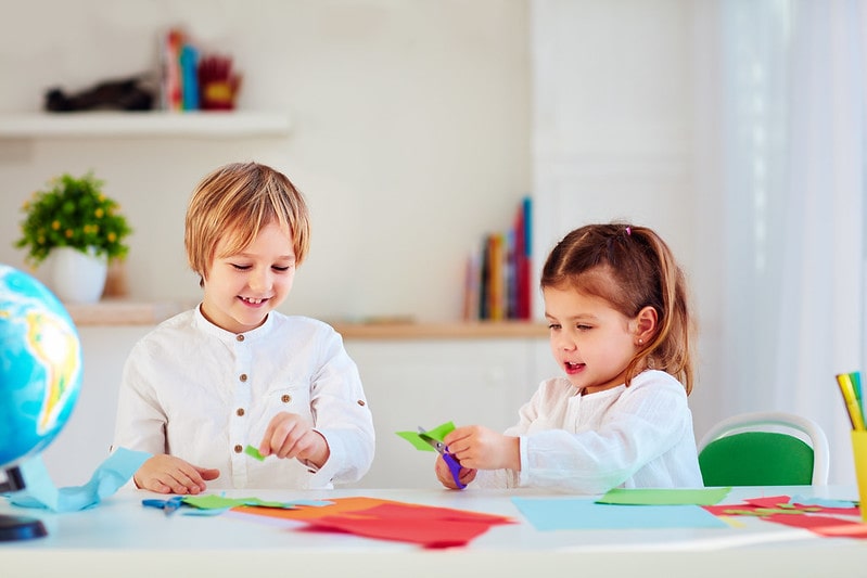 Little boy and girl sat at the table making origami giraffes.