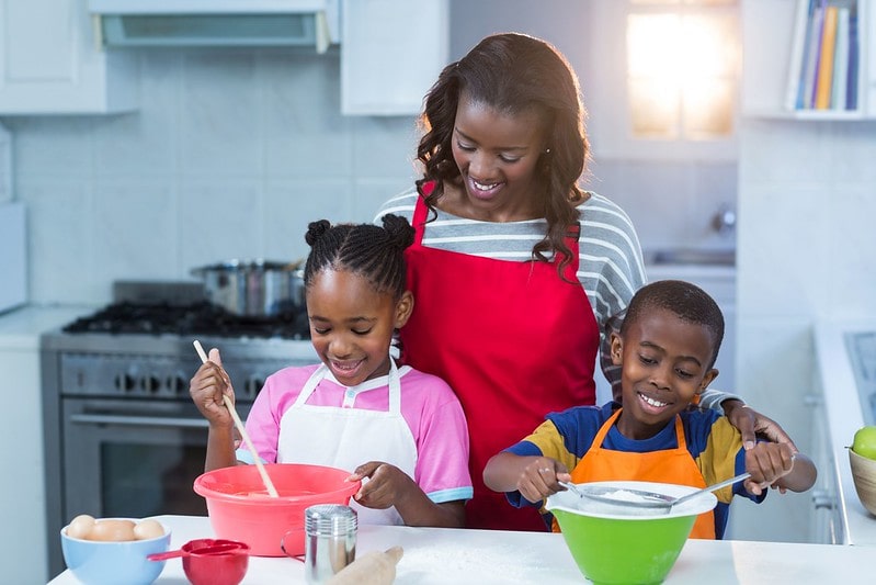 Mum standing with her two children as they bake a cake in the kitchen.