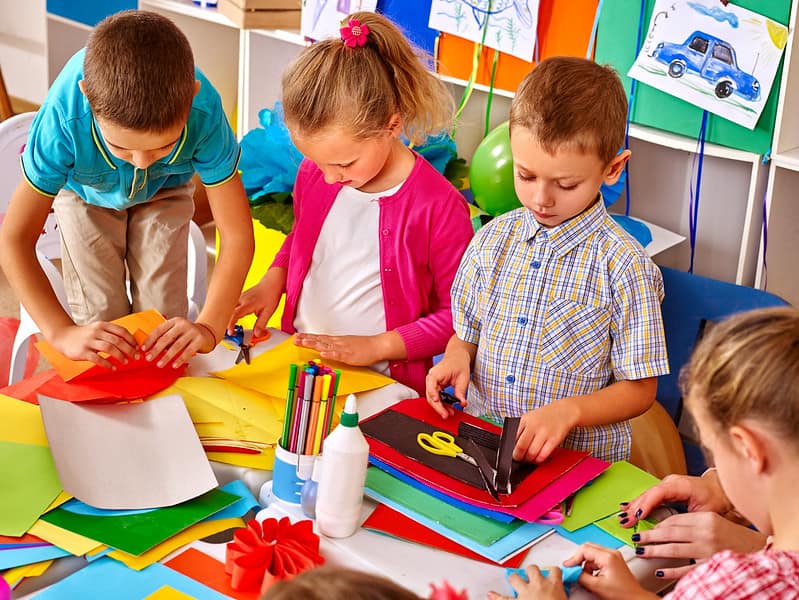 Group of kids in the classroom holding coloured paper to make an origami snake.