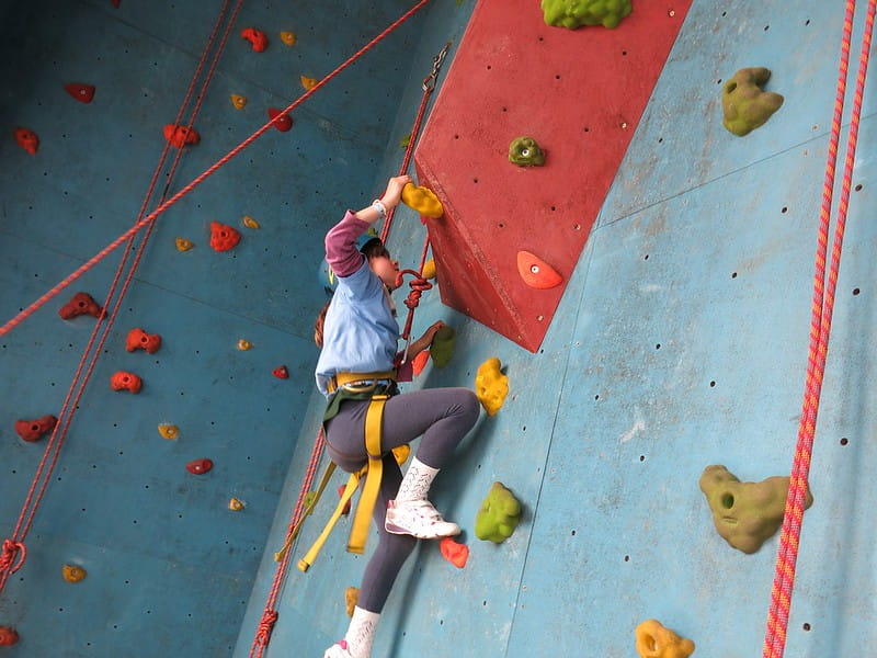 Young girl climbing a tricky part of the rock wall.