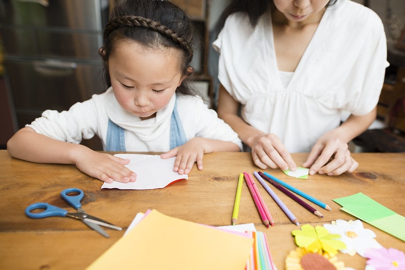 Little girl and her mum folding paper to make an origami shark.