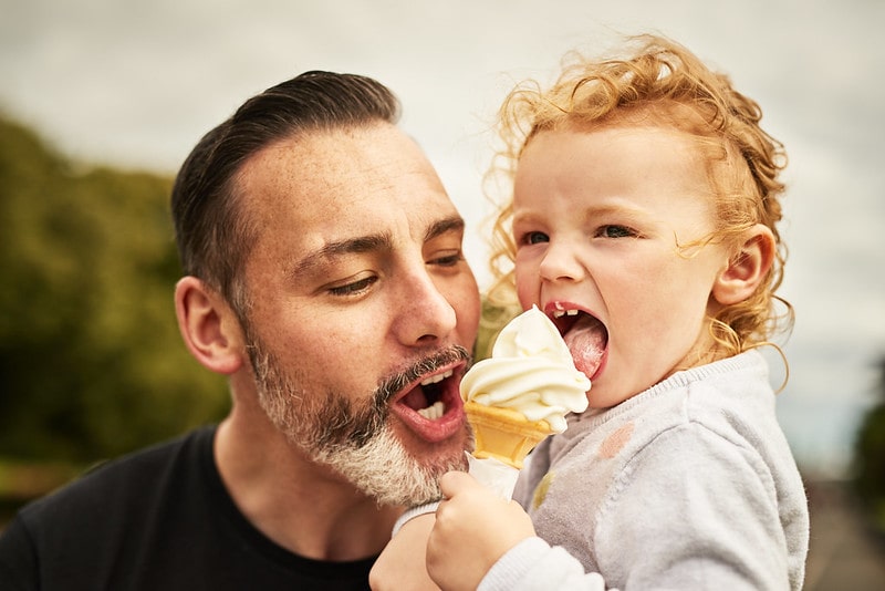 Father and daughter eating a vanilla ice cream cone outside.