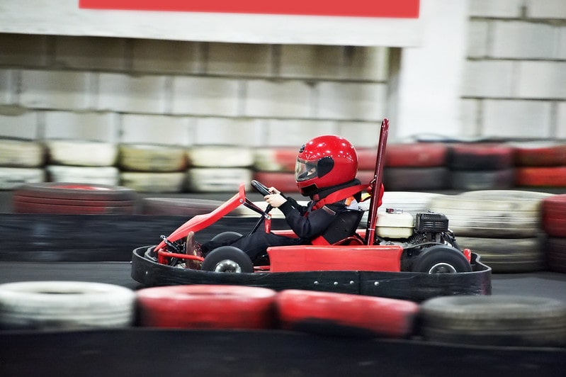 Child driving a go-kart, speeding around the indoor track.