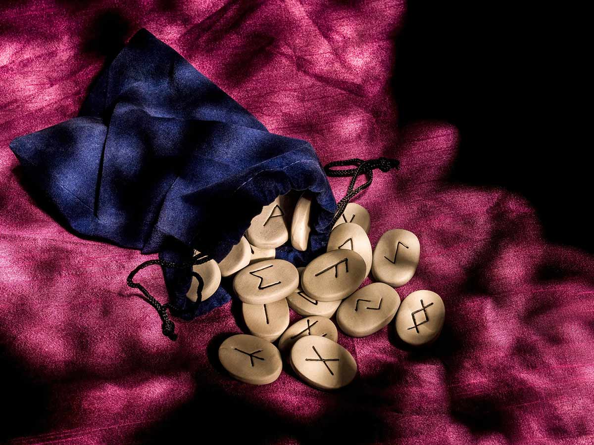Wooden pieces with Anglo-Saxon runes on them coming out a navy velvet pouch.