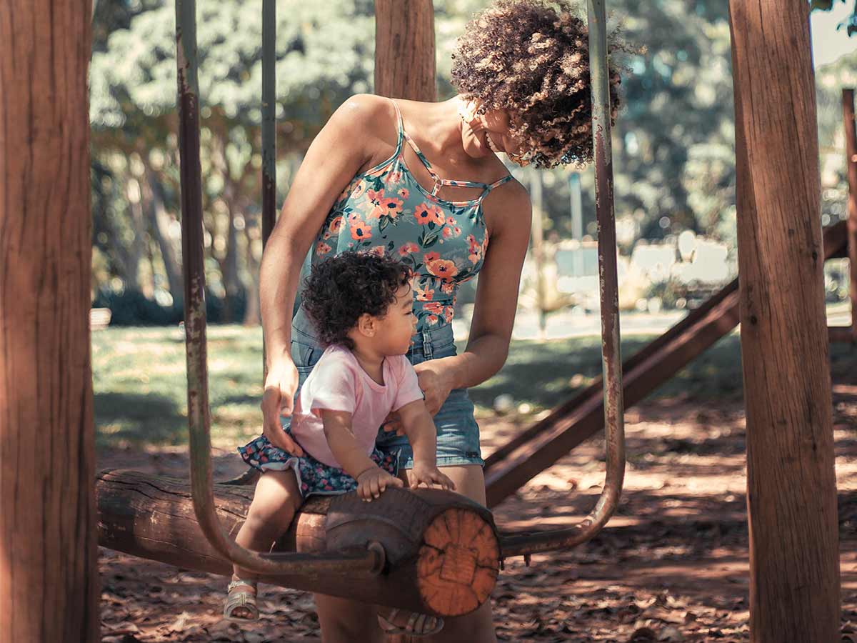 Mum supporting her child on a log swing in the park.