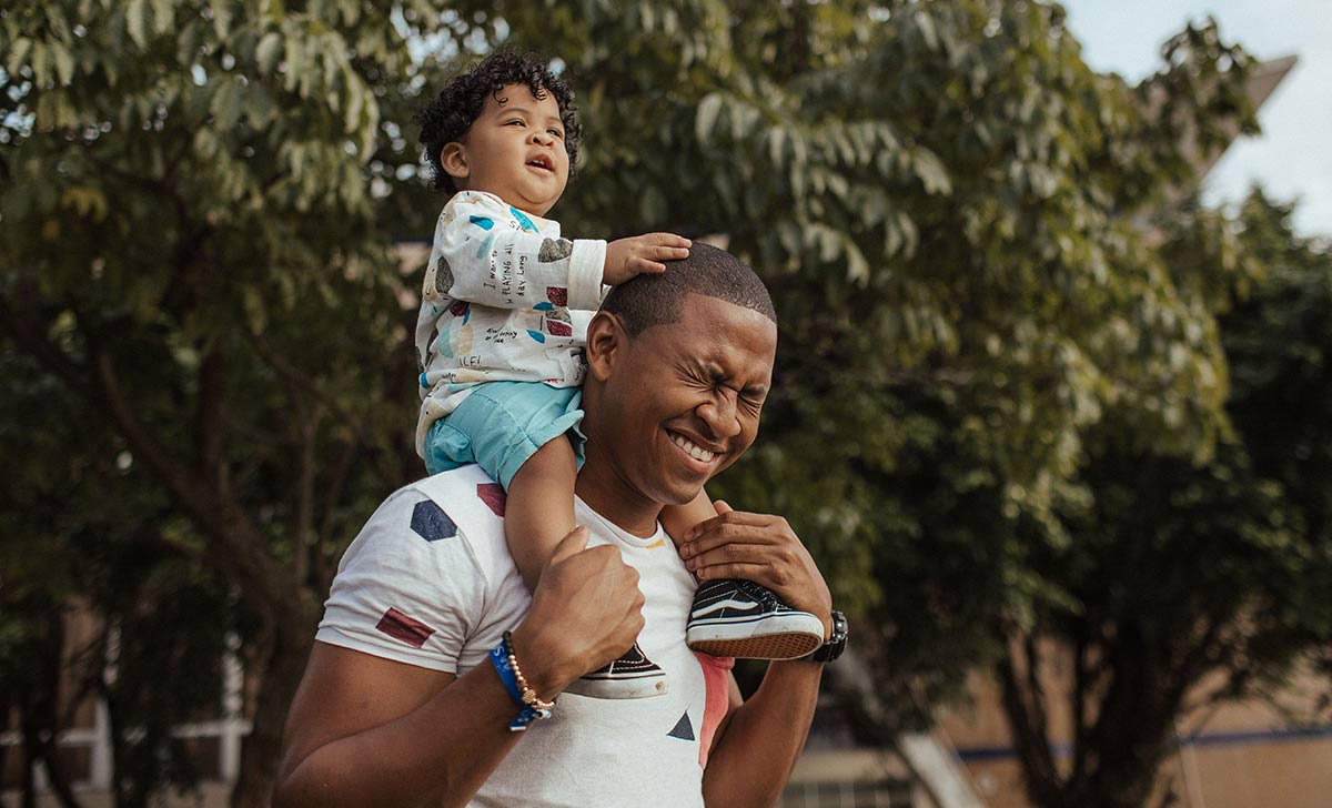 Dad with his young son on his shoulders outside.