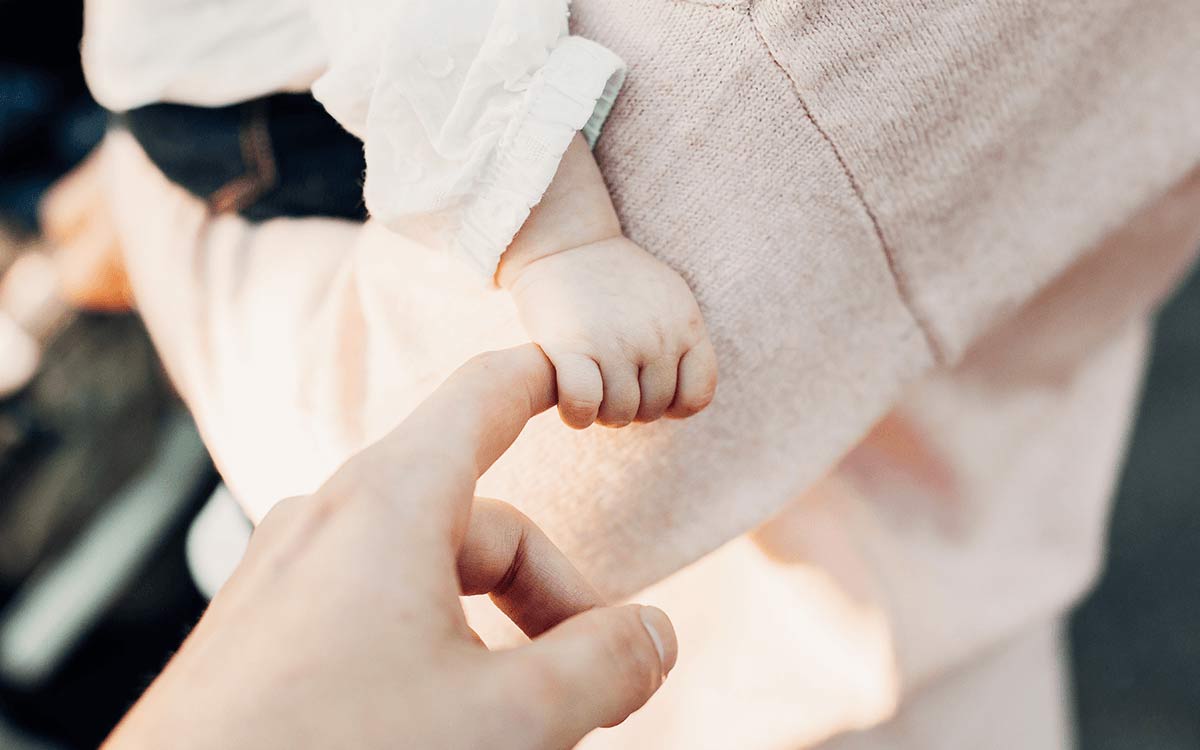 Baby in mum's arms, gripping someone's finger.