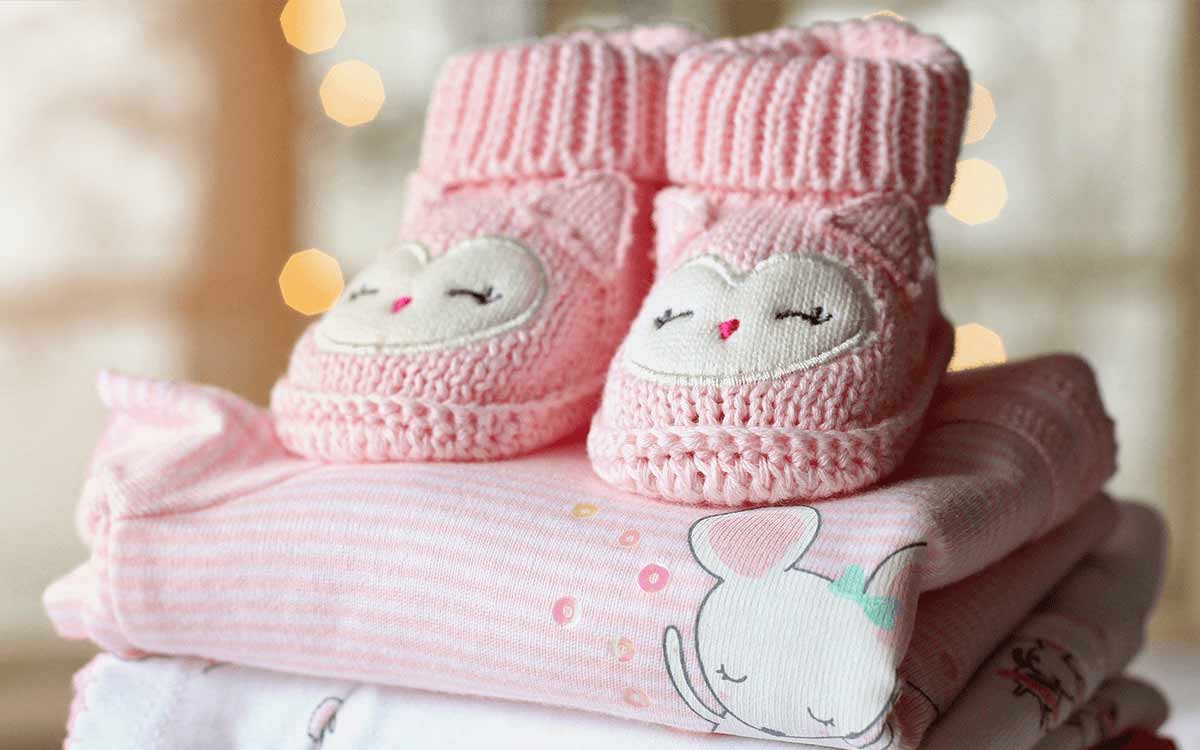 Pair of pink knitted baby boots on top of a pile of pink baby clothes.