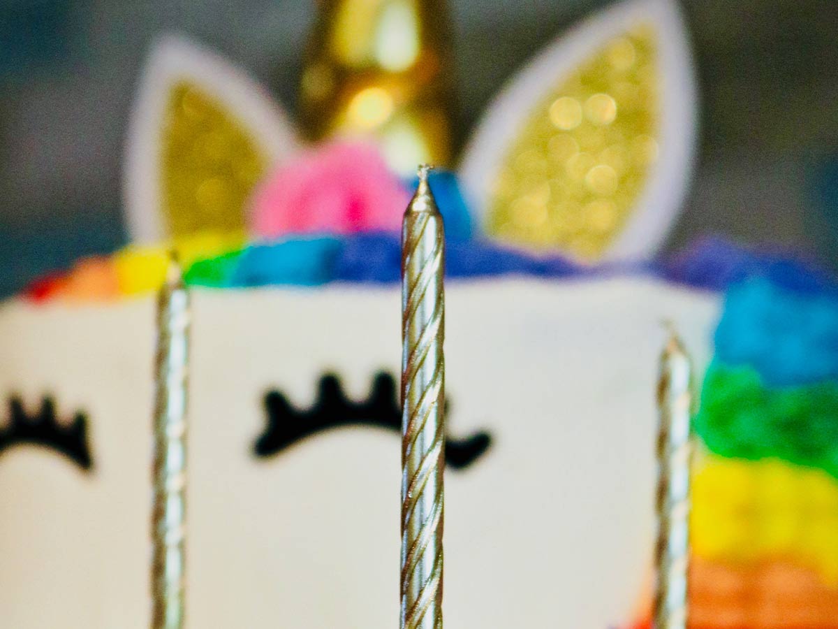 Close up of gold candles in front of a sparkly and colourful unicorn cake.