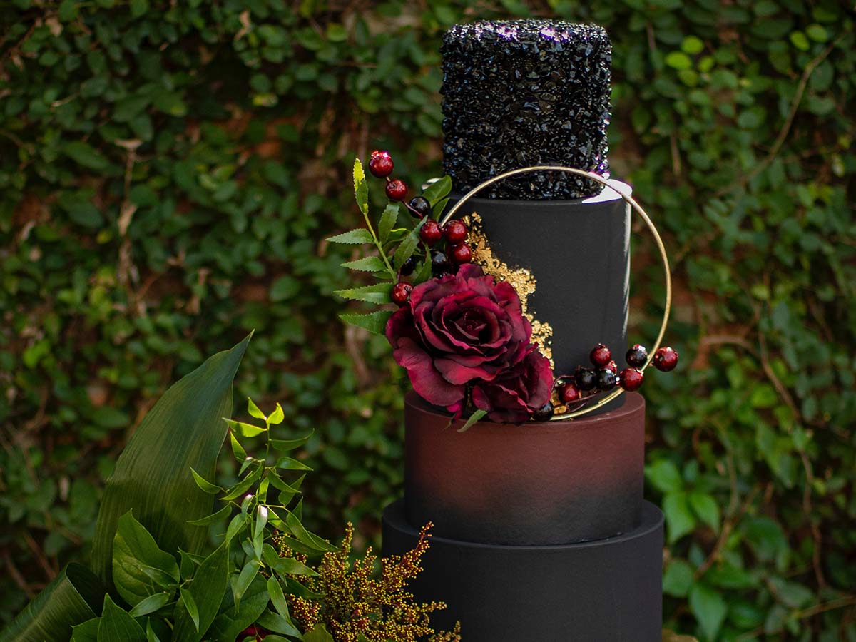 Multi-tiered cake with a dark decoration theme - black and dark red icing and a dark rose.